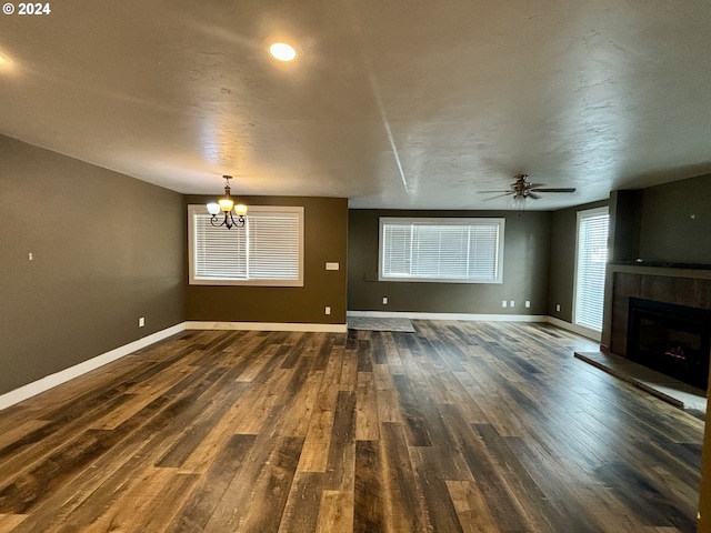 unfurnished living room with a tile fireplace, ceiling fan with notable chandelier, and dark hardwood / wood-style floors