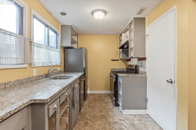 kitchen featuring backsplash, sink, stainless steel gas range, light stone countertops, and range hood