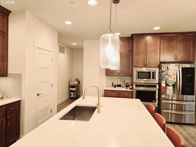 kitchen featuring sink, hanging light fixtures, stainless steel appliances, tasteful backsplash, and light wood-type flooring