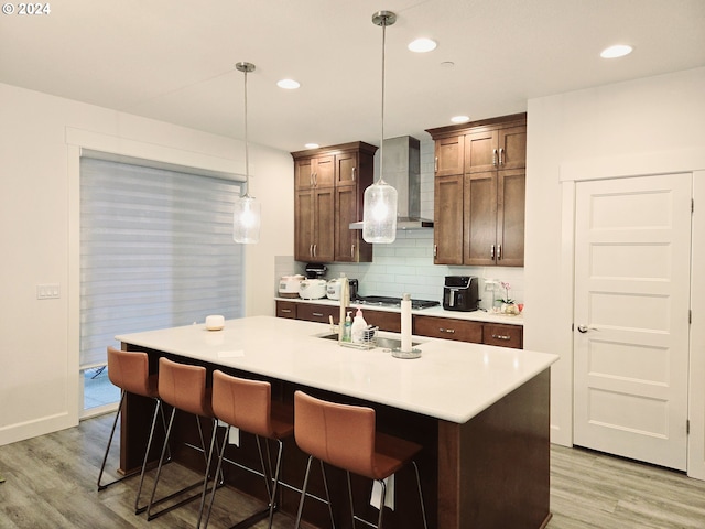 kitchen featuring pendant lighting, hardwood / wood-style flooring, a center island with sink, and wall chimney exhaust hood