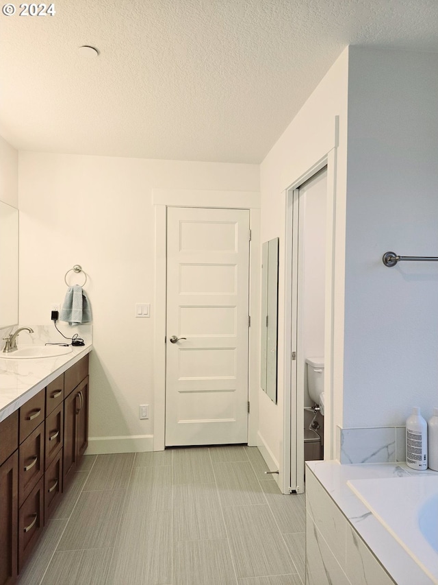 bathroom with a textured ceiling, vanity, toilet, and a bathing tub