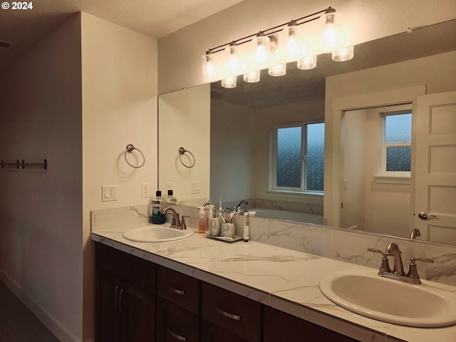 bathroom with a textured ceiling, vanity, and a tub to relax in