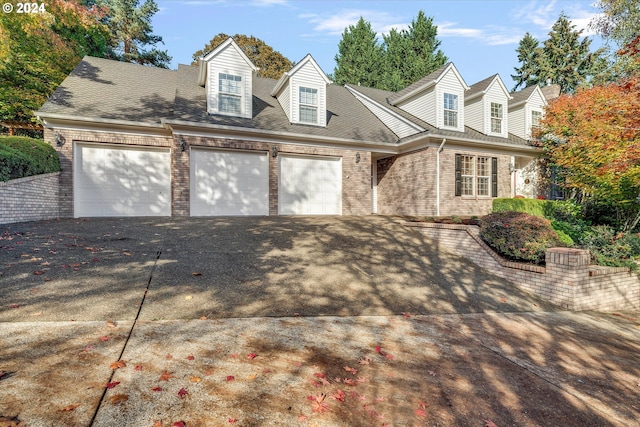 cape cod-style house featuring a garage, brick siding, driveway, and a shingled roof