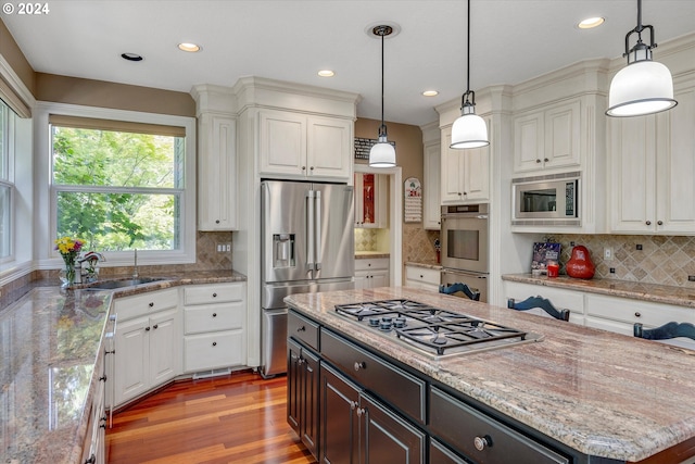 kitchen featuring ornate columns, a center island, stainless steel appliances, light stone counters, and light hardwood / wood-style flooring