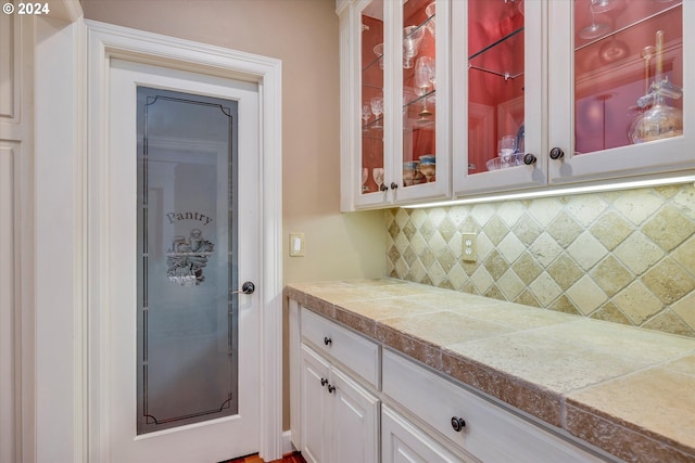 bar with decorative backsplash, white cabinetry, and decorative light fixtures