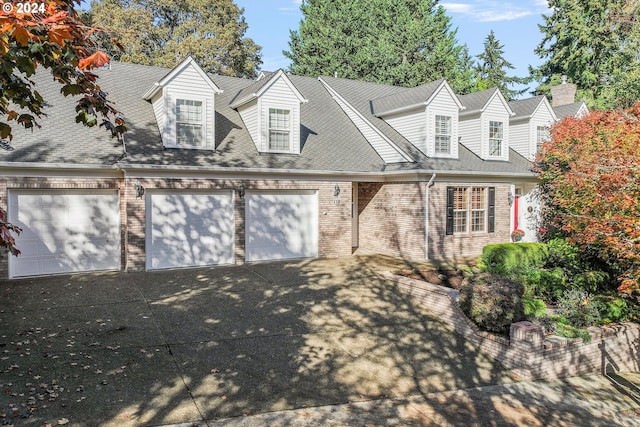 new england style home with a garage, a shingled roof, concrete driveway, and brick siding