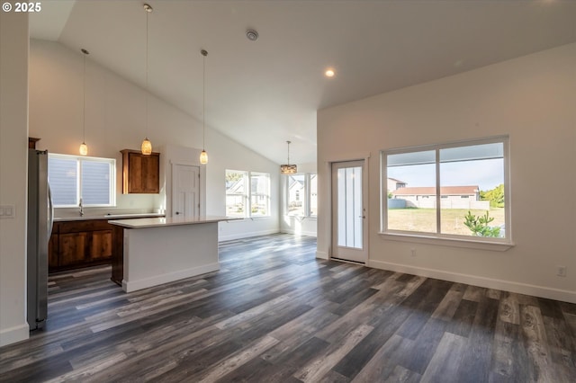 kitchen with sink, stainless steel fridge, a kitchen island, pendant lighting, and dark wood-type flooring