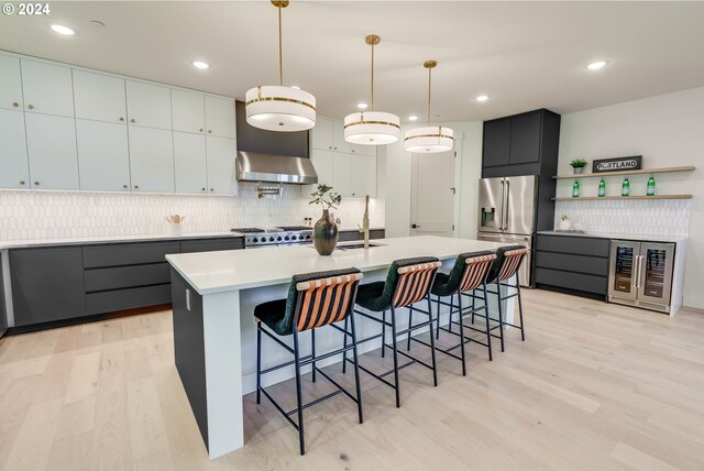 kitchen with appliances with stainless steel finishes, light wood-type flooring, a breakfast bar, decorative light fixtures, and an island with sink