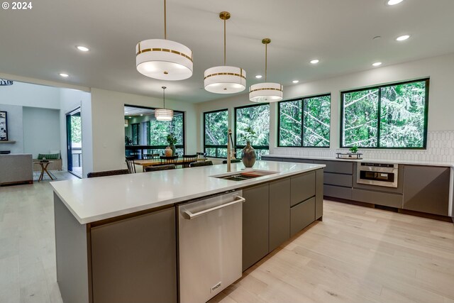 kitchen with appliances with stainless steel finishes, a kitchen island with sink, light hardwood / wood-style flooring, gray cabinets, and hanging light fixtures