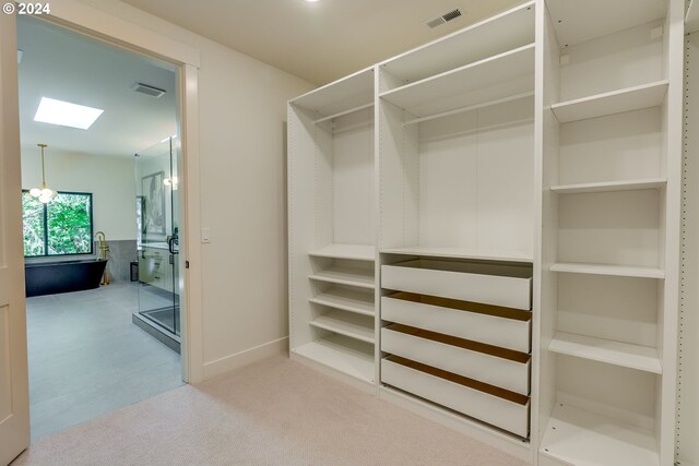 walk in closet featuring an inviting chandelier, light colored carpet, and a skylight