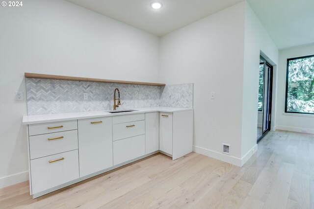 kitchen featuring white cabinets, light hardwood / wood-style floors, sink, and tasteful backsplash