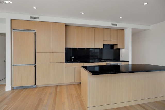 kitchen with light wood-type flooring, a center island, light brown cabinetry, and paneled built in fridge