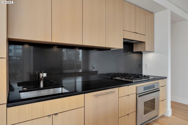 kitchen featuring appliances with stainless steel finishes, decorative backsplash, light wood-type flooring, and light brown cabinets