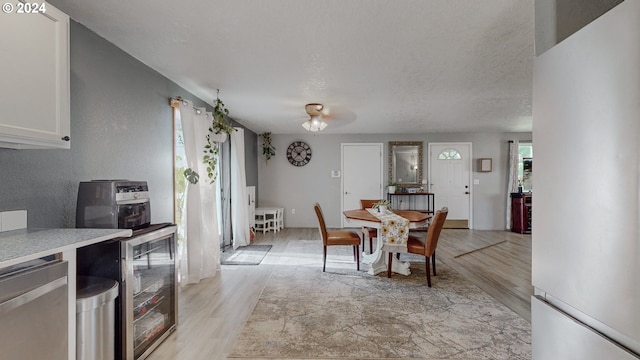 dining room featuring ceiling fan, beverage cooler, light hardwood / wood-style flooring, and a textured ceiling