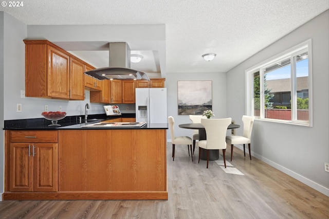 kitchen featuring white refrigerator with ice dispenser, a textured ceiling, island range hood, kitchen peninsula, and light hardwood / wood-style floors