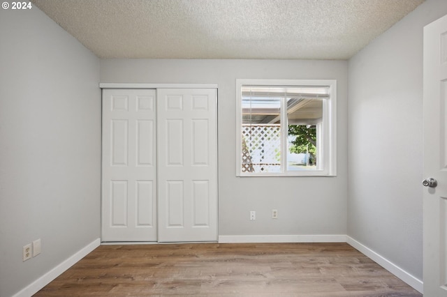 unfurnished bedroom with a textured ceiling, a closet, and light hardwood / wood-style floors