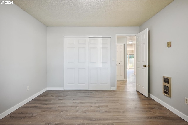 unfurnished bedroom featuring a closet, hardwood / wood-style flooring, heating unit, and a textured ceiling