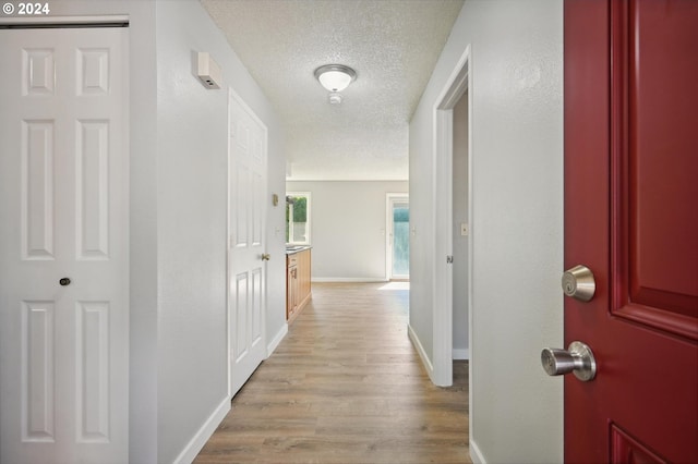 corridor with light wood-type flooring and a textured ceiling