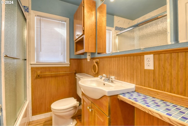 full bathroom with vanity, combined bath / shower with glass door, wood walls, and toilet