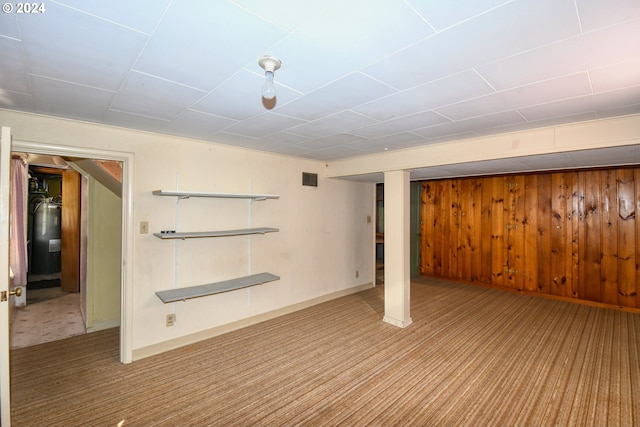 basement featuring wood walls, electric water heater, and carpet