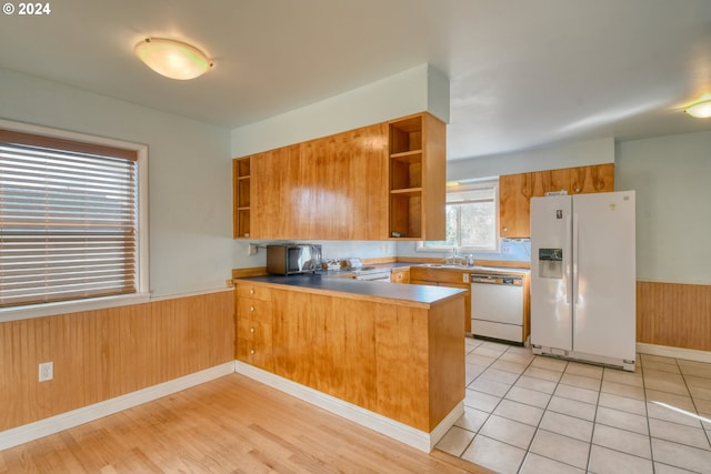 kitchen with wooden walls, kitchen peninsula, white appliances, and light tile patterned floors