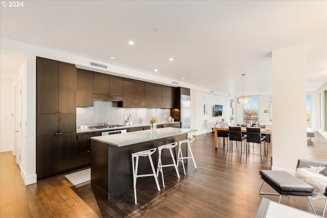 kitchen featuring a center island with sink, dark hardwood / wood-style floors, decorative light fixtures, dark brown cabinetry, and a breakfast bar area