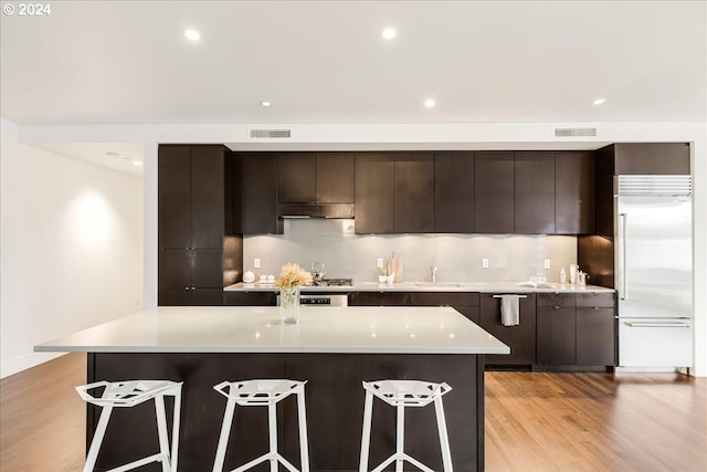 kitchen with built in fridge, a center island, dark brown cabinetry, and light hardwood / wood-style floors