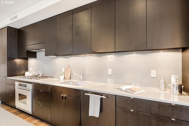 kitchen featuring light wood-type flooring, dark brown cabinetry, white oven, stainless steel gas cooktop, and sink