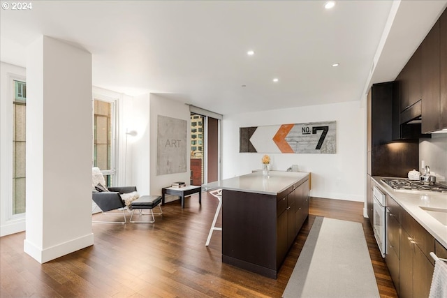 kitchen with a kitchen breakfast bar, dark brown cabinets, stainless steel gas cooktop, dark wood-type flooring, and a kitchen island