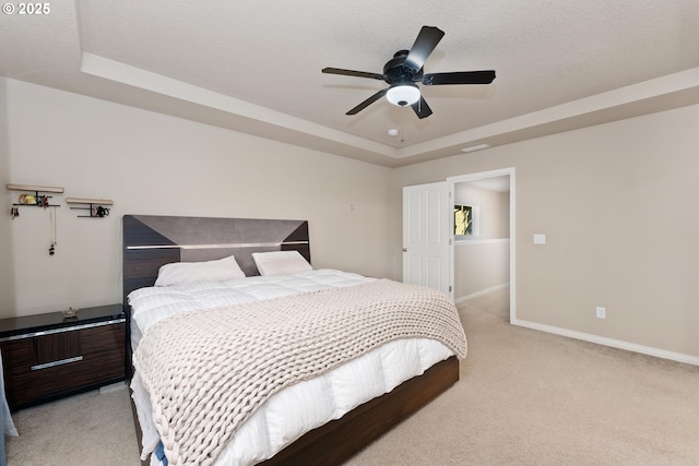 bedroom featuring ceiling fan, a tray ceiling, light carpet, and a textured ceiling