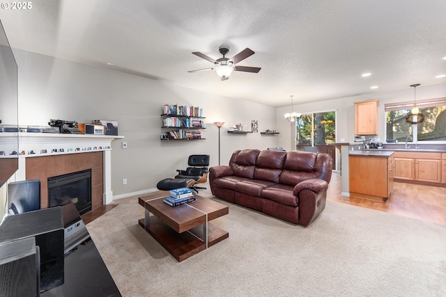 living room featuring sink, a fireplace, ceiling fan with notable chandelier, and a textured ceiling