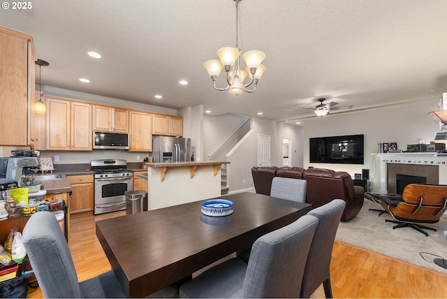 dining area with sink, a fireplace, a textured ceiling, ceiling fan with notable chandelier, and light wood-type flooring