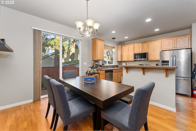 dining area with a notable chandelier, light hardwood / wood-style flooring, sink, and a healthy amount of sunlight