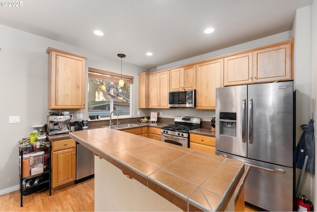 kitchen featuring sink, hanging light fixtures, light hardwood / wood-style flooring, tile counters, and stainless steel appliances