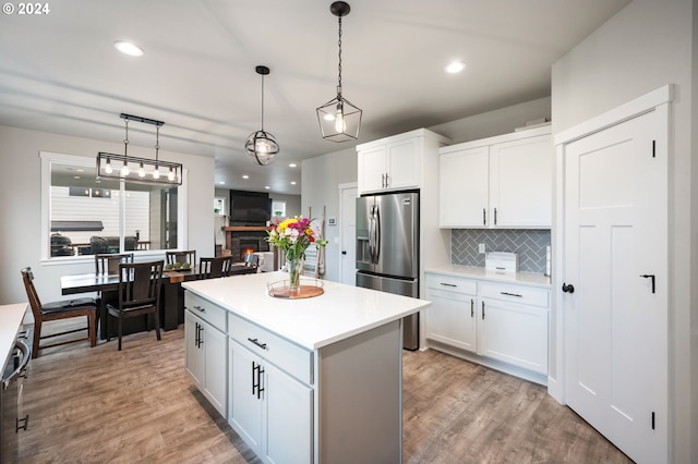 kitchen with light wood finished floors, a center island, stainless steel fridge with ice dispenser, light countertops, and tasteful backsplash