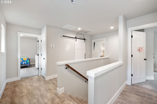 corridor featuring light wood-type flooring, baseboards, an upstairs landing, and a barn door