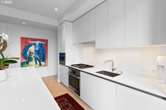 kitchen with stainless steel appliances, sink, light wood-type flooring, and white cabinetry