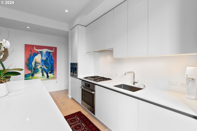 kitchen with stainless steel appliances, a sink, white cabinetry, light countertops, and modern cabinets