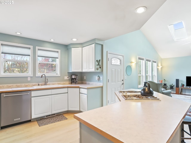 kitchen featuring lofted ceiling with skylight, sink, stainless steel appliances, light hardwood / wood-style floors, and white cabinets