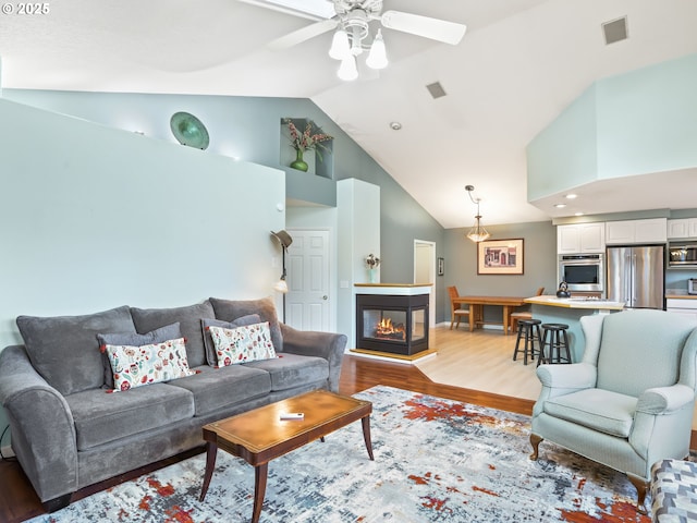 living room featuring a multi sided fireplace, ceiling fan, high vaulted ceiling, and light hardwood / wood-style flooring