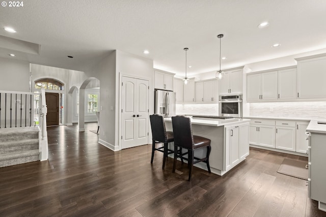 kitchen with appliances with stainless steel finishes, a center island, dark hardwood / wood-style flooring, white cabinetry, and decorative light fixtures