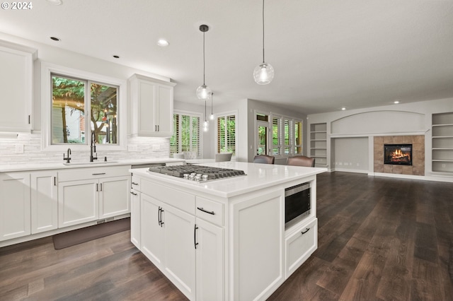 kitchen with appliances with stainless steel finishes, sink, white cabinetry, a tiled fireplace, and pendant lighting