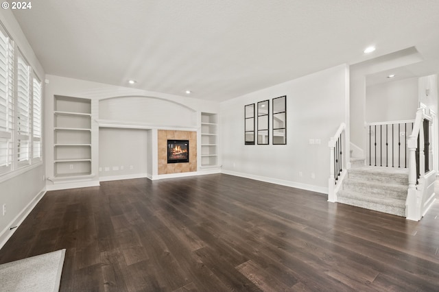 unfurnished living room with dark wood-type flooring, built in features, and a tile fireplace