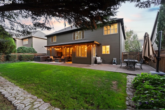 back house at dusk featuring outdoor lounge area, a patio area, and a lawn