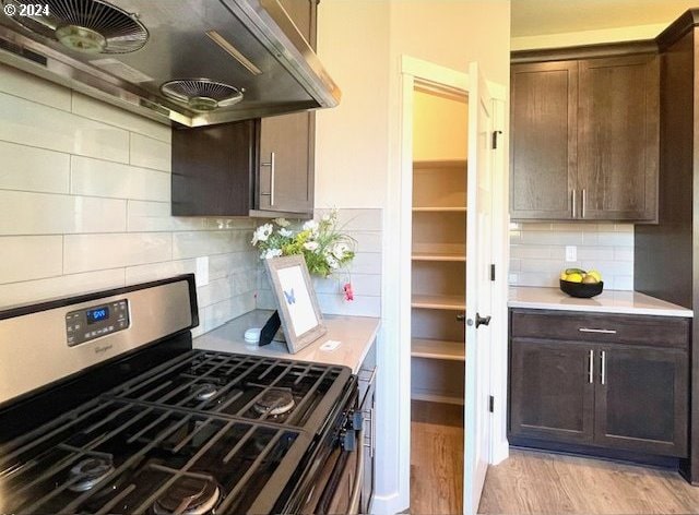 kitchen featuring light wood-type flooring, ventilation hood, stainless steel gas range, and dark brown cabinetry