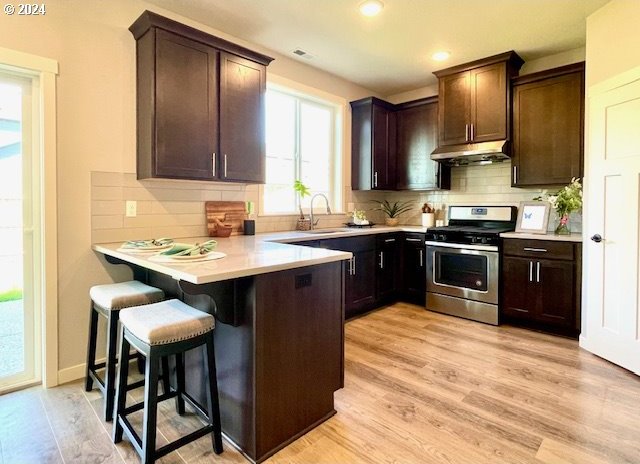 kitchen with stainless steel range, light hardwood / wood-style floors, a breakfast bar, kitchen peninsula, and sink