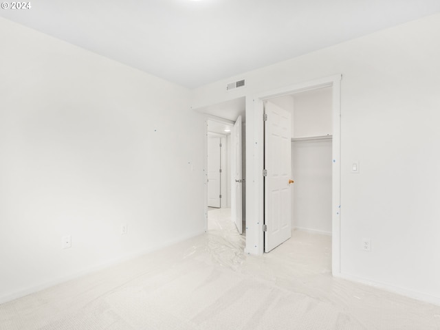 unfurnished bedroom with a spacious closet, light colored carpet, and a closet