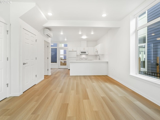 kitchen with light hardwood / wood-style flooring, kitchen peninsula, a wall mounted air conditioner, white cabinets, and white appliances