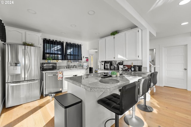 kitchen with kitchen peninsula, light hardwood / wood-style flooring, a breakfast bar area, black appliances, and white cabinetry