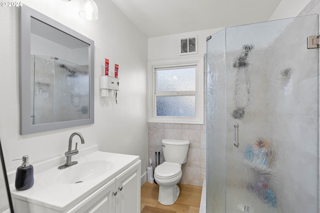 bathroom featuring toilet, vanity, wood-type flooring, tile walls, and an enclosed shower